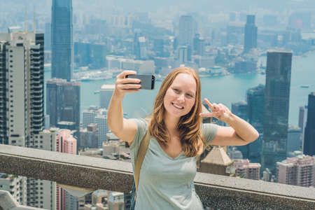 Hong Kong Victoria Peak woman taking selfie stick picture photo with smartphone enjoying view over Victoria Harbour. Viewing platform on top of Peak Tower, HK. Defocused background.Travel asia concept.の写真素材