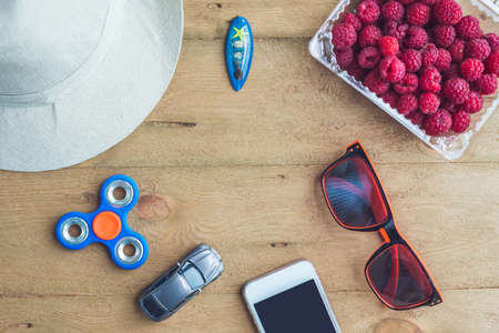 Summer holiday, vacation, relaxation concept. Raspberries, hat, mobile phone, smartphone, spinner, sunglasses from above, top view, flat lay on wooden background. Colorful background with free text copy space. Summer vibes concept.の写真素材