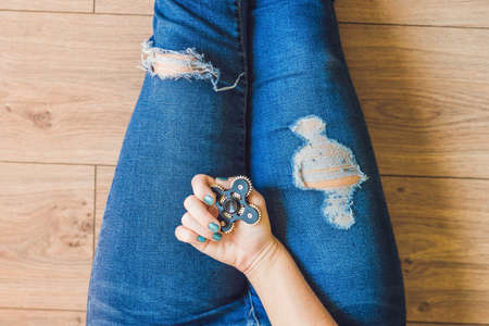 Girl teenager in holey jeans holds in hands and plays with spinner.の写真素材