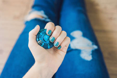 Girl teenager in holey jeans holds in hands and plays with spinner.