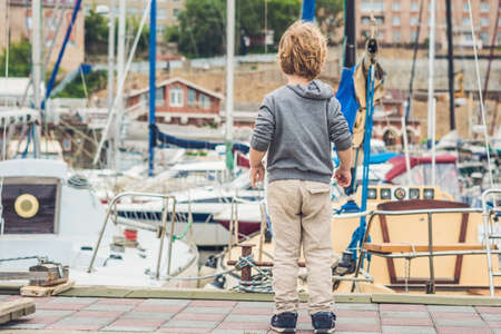 Cute blond boy looking at yachts and sailboats.の写真素材