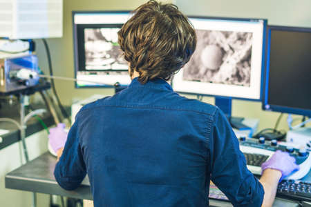Scientist works at a electron microscope control pannel with two monitors in front of him.の写真素材