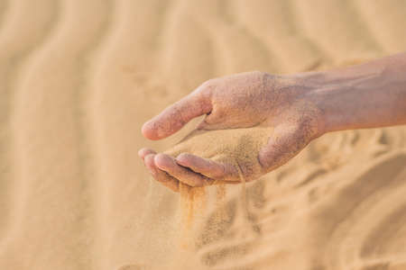Desert, sand puffs through the fingers of a man's hand.の写真素材