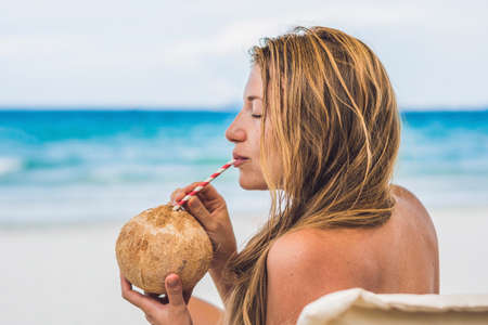 Young woman drinking coconut milk on Chaise-longue on beach. Dream scape Escape with beauty girl....