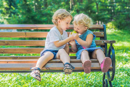 Toddlers boy and girl sitting on a bench by the sea and eat an apple.の写真素材