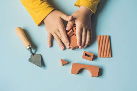 Close up of child's hands playing with real small clay bricks at the table. Toddler having fun and building out of real small clay bricks. Early learning. Developing toys. Construction concept.の写真素材