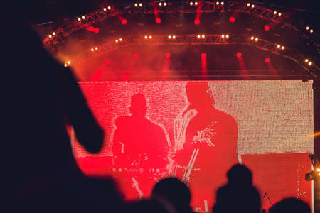 Silhouette of a big crowd at concert against a brightly lit stage. Night time rock concert with...