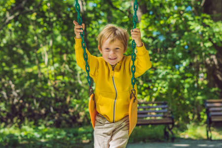 A boy in a yellow sweatshirt sits on a swing on a playground in autumn.の写真素材