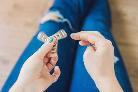 Girl teenager in holey jeans holds in hands and plays with spinner.の写真素材