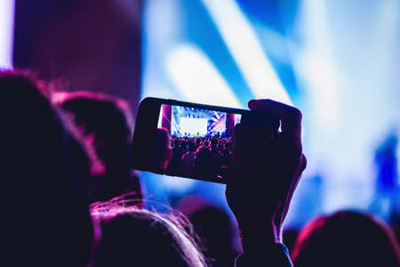 People enjoying rock concert and taking photos with cell phone at music festival.の写真素材