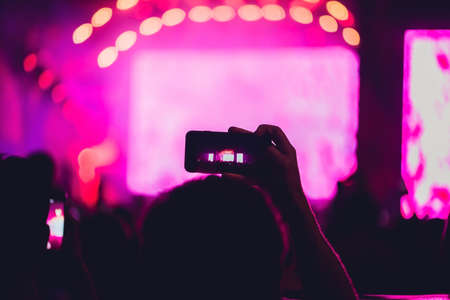 People enjoying rock concert and taking photos with cell phone at music festival.の写真素材