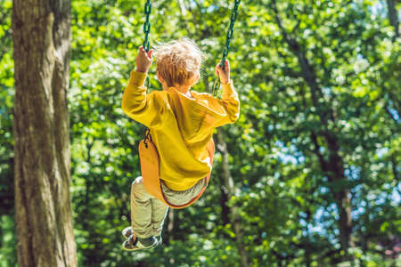 A boy in a yellow sweatshirt sits on a swing on a playground in autumn.の写真素材