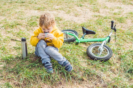 Portrait of Adorable cute boy resting and drinking tea from a thermos in the beauty autumn park.の写真素材