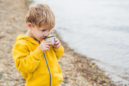 Portrait of Adorable cute boy resting and drinking tea from a thermos in the beauty autumn park.の写真素材
