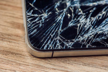 Smartphone display with broken glass on a wodden table.