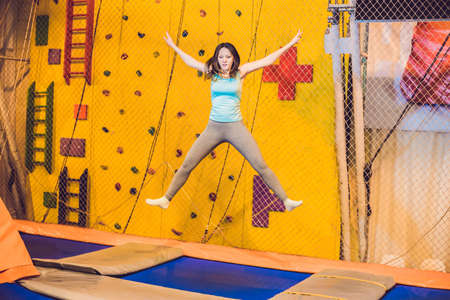 Young woman sportsman jumping on a trampoline in fitness park and doing exersice indoors.の写真素材