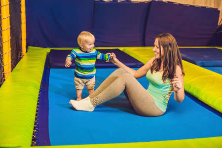 Mother And her son jumping on a trampoline in fitness park and doing exersice indoors.の写真素材