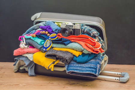 Open travel bag with clothes, film camera on floor.