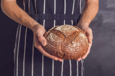 Baker man holding homemade rustic wheat bread in hands. Selective focus.の写真素材