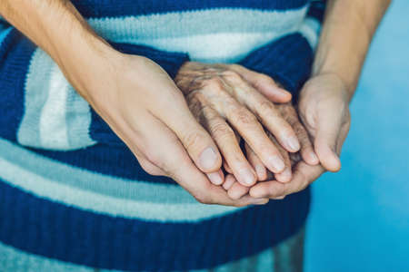 Hands of an old woman and a young man. Caring for the elderly. close up.の写真素材