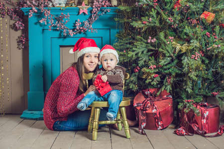 Portrait of happy mother and adorable baby celebrate Christmas. New Year's holidays. Toddler with mom in the festively decorated room with Christmas tree and decorations.の写真素材