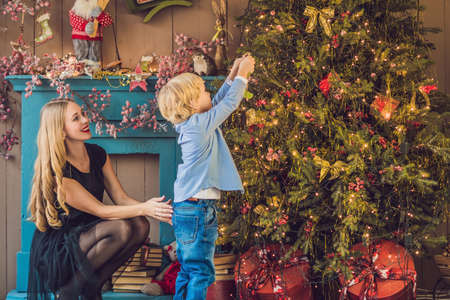 Portrait of happy mother and adorable boy celebrate Christmas. New Year's holidays. Toddler with mom in the festively decorated room with Christmas tree and decorations.の写真素材