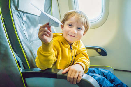 Little boy play with paper plane in the commercial jet airplane flying on vacation.の写真素材