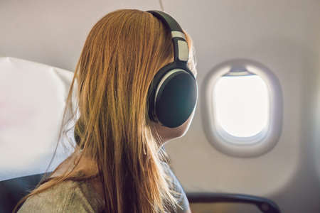 Passenger in airplane using headphones. Woman in plane cabin using smart device listening to music on headphones.の写真素材