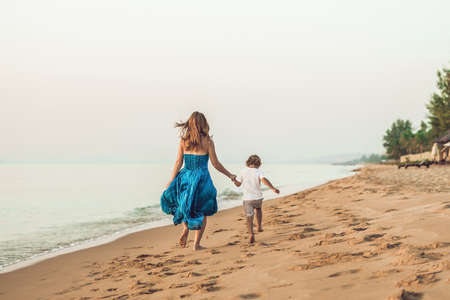 Portrait of smiling young mother with little child running on the beach.の写真素材