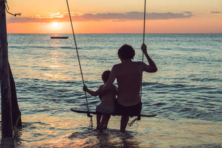 silhouette of father and son play swing sunset background.の写真素材