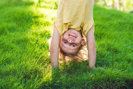 Portraits of happy kids playing upside down outdoors in summer park walking on hands.