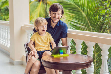 father and son in the tropics talking with friends and family on video call using a tablet and...
