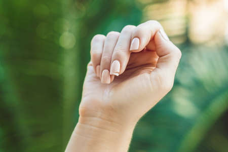 Broken nail on a woman's hand with a manicure on a green background.