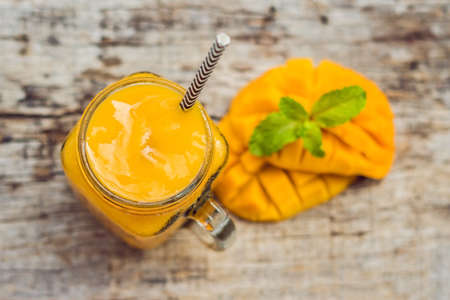 Mango smoothie in a glass Mason jar and mango on a green background. Mango shake. Tropical fruit concept.の写真素材