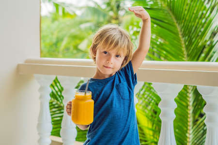The boy holds mason jar of mango smoothies in his hand and shows how he grew up thanks to vitamins...