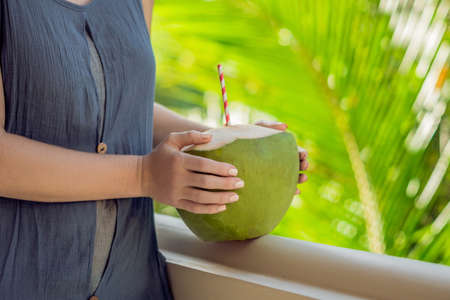 Coconut in beautiful female hands on a green background. The Benefits of Coconut Water Concept.