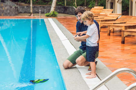 Father and son playing with a remote controlled boat in the pool.の写真素材