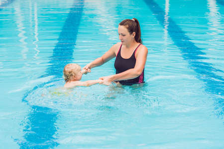 Young mother teach her little son, how to swim in a swimming pool.の写真素材