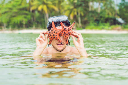 Happy young scuba diver holding sea star, smiling, looking at camera.の写真素材