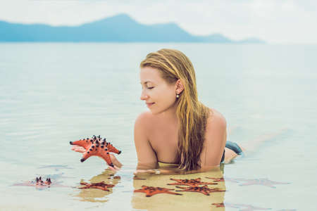 Young woman in the sea with red starfishes.
