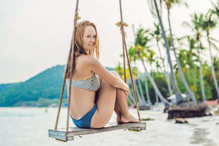 Vacation concept. Happy young woman sitting on swing enjoying sea view.の写真素材