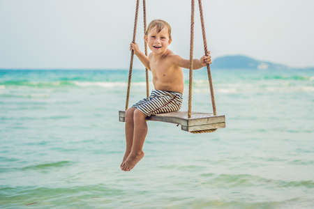Happy boy sit on swing at the sea shore on sunset.の写真素材