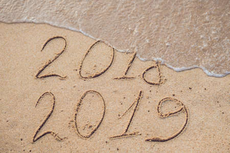 New Year 2019 is coming concept - inscription 2018 and 2019 on a beach sand, the wave is almost covering the digits 2018.の写真素材