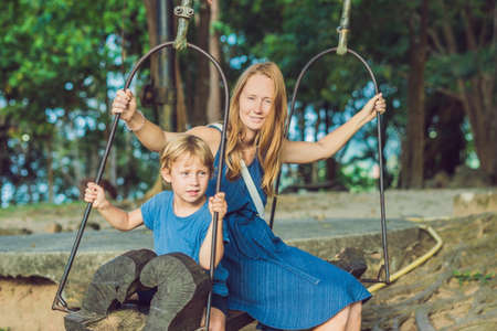 Mom and son swinging on an old swing against the background of the roots of the tree.の写真素材