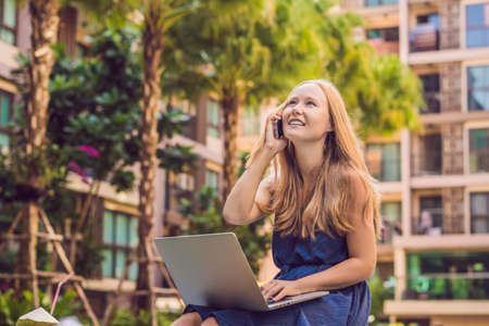 Young female freelancer sitting near the pool with her laptop in the hotel browsing in her smartphone. Busy at holidays. Distant work concept. Copy space for your text.の写真素材