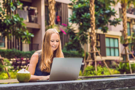 Young female freelancer sitting near the pool with her laptop in the hotel browsing in her smartphone. Busy at holidays. Distant work concept. Copy space for your text.の写真素材