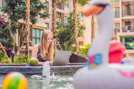 Young female freelancer sitting near the pool with her laptop in the hotel browsing in her smartphone. Busy at holidays. Distant work concept. Copy space for your text.の写真素材