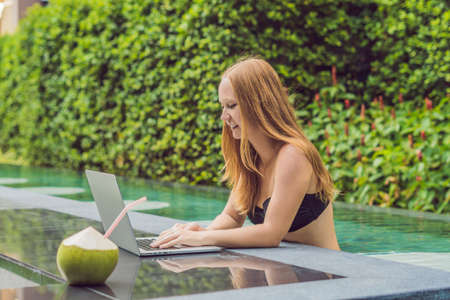 Young female freelancer sitting near the pool with her laptop in the hotel browsing in her smartphone. Busy at holidays. Distant work concept. Copy space for your text.の写真素材