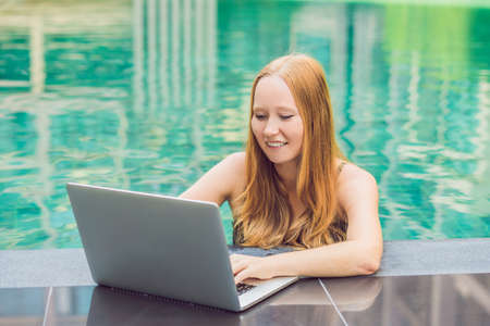 Young female freelancer sitting near the pool with her laptop in the hotel browsing in her smartphone. Busy at holidays. Distant work concept. Copy space for your text.の写真素材