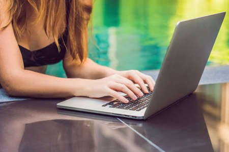 Young female freelancer sitting near the pool with her laptop in the hotel browsing in her smartphone. Busy at holidays. Distant work concept. Copy space for your text.の写真素材